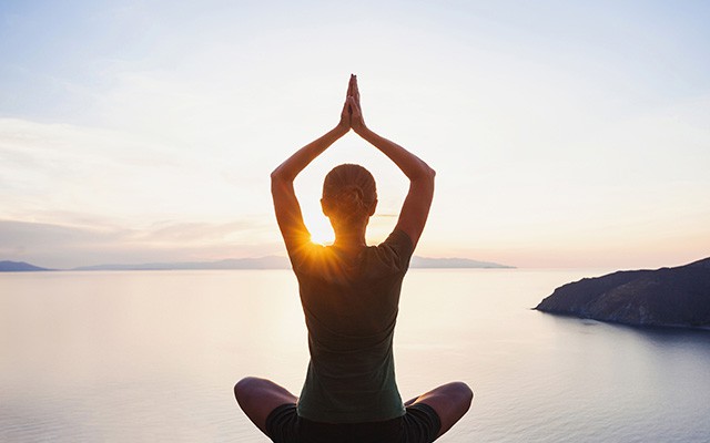 Eine Frau praktiziert Yoga am Meer während des Sonnenuntergangs.